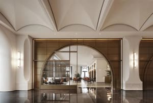 Elegant hotel lobby with a grand archway entrance, comfortable seating areas, and dining tables, set against a neutral background