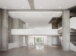 Spacious modern living space with high ceilings, concrete walls and floors, and two dining tables with chairs
