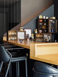 A cozy kitchen with wooden floors, cabinets, and countertops, featuring a dining table and chairs, with various objects and vases scattered throughout the space