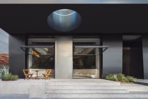 Modern building exterior with a black facade, a large circular window, and two chairs and three potted plants outside