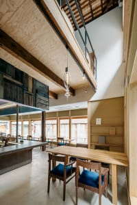 A modern restaurant interior with wooden floors and walls, featuring a large dining table, chairs, and a countertop with a sink