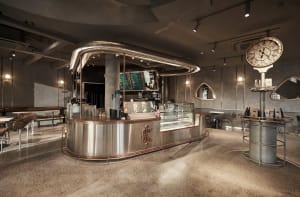 A modern coffee shop interior with a stainless steel counter, displaying various drinks and food items, in a warm and inviting atmosphere