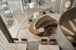 A modern restaurant interior with a curved bench seating area, wood accents, and metal elements, surrounded by chairs and dining tables