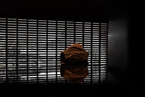 A brown rock sits on a reflective glass table in an indoor space with vertical blinds on the wall