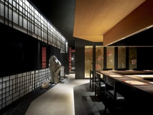 A modern Asian restaurant with tile flooring, tables, chairs, and potted plants, complemented by artwork on the walls