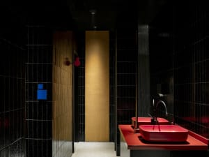 A well-lit bathroom with two sinks, one with a blue button, and tiled walls
