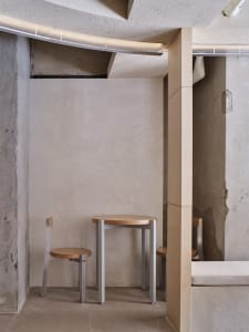 Dining area with concrete walls, a small table, and three chairs, accompanied by a bench in a modern and industrial space