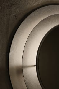 A bathroom with a round mirror on the wall reflecting a decorative piece, in a clean and well-organized space