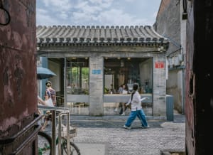 A lively Asian restaurant with a brick facade, featuring a large archway entrance, dining tables, chairs, and potted plants, with people enjoying their meals