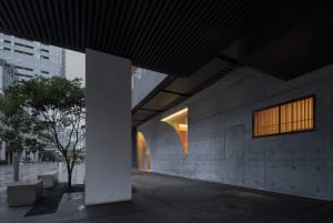 A modern building with a concrete facade, featuring a large window and nighttime lighting