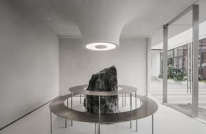 A modern living space features a large rock at the center of a metal table, surrounded by a contemporary setting, possibly a lobby or lounge