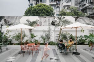 Outdoor dining area with tables, chairs, umbrellas, and greenery, featuring a casual and inviting atmosphere