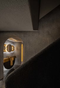 Modern bathroom with a black countertop, gold faucet, and carpeted staircase leading to another level