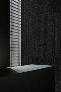 Dark interior space with a stone wall featuring two windows, one on each side, and a lack of natural light