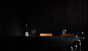 Dark dining area with two chairs and a table, wine glasses, and a bottle of wine, creating an intimate and sophisticated atmosphere