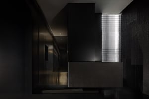 Dark modern kitchen dining space with a black countertop, a dining table, and a chair, surrounded by walls and minimal decor