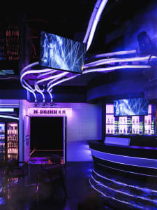 A stylish bar area with purple lighting, multiple TV screens, and comfortable seating for patrons