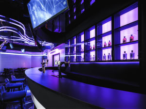 A cozy bar area with a wooden counter, chairs, and bottles, creating a relaxed atmosphere