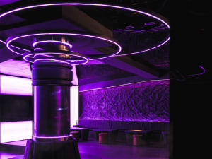 Modern bar area with a purple-lit circular feature, chairs, and dining tables, surrounded by a stylish and sophisticated atmosphere