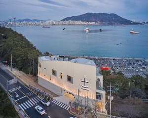 A modern building with a glass facade and multiple windows, situated near water, with cars parked outside, suggesting a commercial or public space