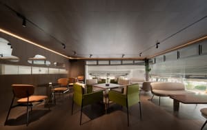 A restaurant interior with wooden floors and walls, featuring green upholstered chairs, potted plants, and a warm atmosphere