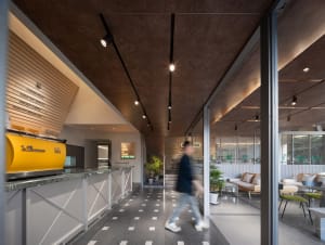 A modern office space with a large open area, a counter, and a dining table, featuring a combination of tiles and carpet flooring, neutral walls, and comfortable seating arrangements