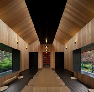 Open living area with wooden floors and walls, featuring two dining tables, chairs, and decorative books, with a warm and inviting atmosphere