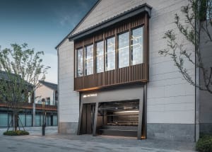 A modern storefront with a black awning, stone and glass elements, and large windows providing natural light into the interior spaces