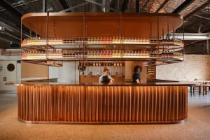 A casual bar area with a long wooden counter, bottles, and staff serving patrons in a relaxed dining environment
