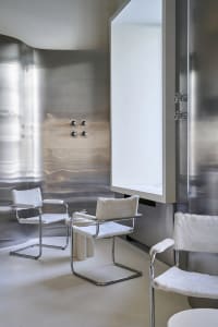 A minimalist bathroom with a large mirror, two chairs, and a sink, featuring a clean and white design