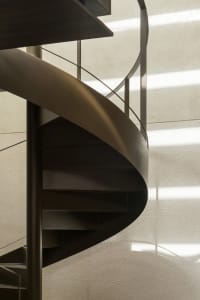 A modern metal staircase near a window, illuminated by natural light, with a sense of depth and complexity within the structure