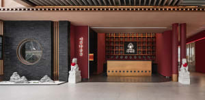 Modern hotel lobby with a large wooden desk, chairs, and a unique wall pattern, featuring a statue near the entrance