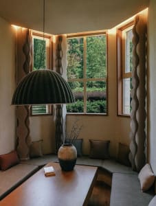 A well-lit living area with neutral tones, wood, and stone, featuring a dining table, chairs, couches, and a large window for natural light