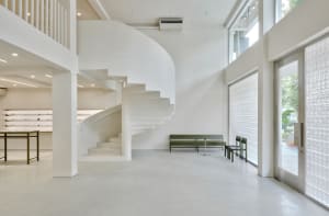 Empty minimalist room with a spiral staircase made of concrete and metal railing, surrounded by white walls and floor