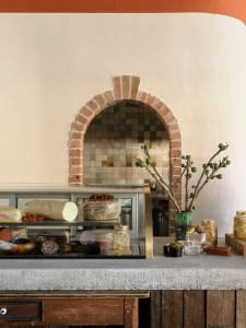 Cozy cafe interior with a brick wall, display case filled with food items, and bottles placed around the area