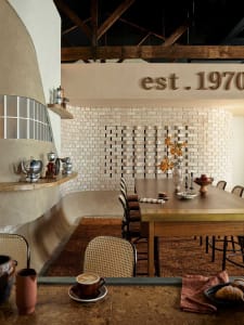 A well-lit dining area with a wooden table surrounded by chairs, featuring cups, bowls, and vases, creating a warm and inviting atmosphere