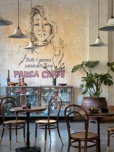 Warm and inviting coffee shop interior with tables, chairs, potted plants, artwork, and a painting of a woman holding a cup