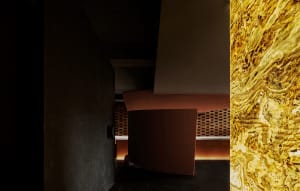 Darkened room with a large red wall, possibly marble, and two chairs placed near the wall, creating a modern and luxurious atmosphere