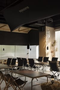 Dimly lit restaurant interior with black chairs, potted plants, and a dining area with tables arranged in rows