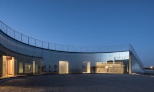 Modern art gallery with a circular building featuring a glass exterior, chairs, and decorative umbrellas