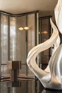 A modern interior space with a large marble sculpture, glass wall, and two lights, creating a contemporary atmosphere