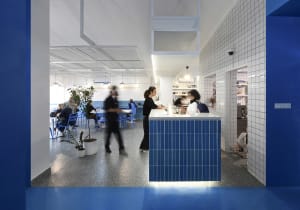 Casual restaurant interior with a blue countertop, blue walls, and modern blue tiles, featuring a bustling atmosphere with people ordering food