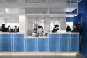 A bustling restaurant counter with people waiting in line to order food and drinks, surrounded by cups and a lively atmosphere