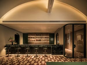 A stylish bar area in a restaurant with a marble countertop, mirror, and stools, offering a selection of beverages