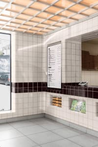 Modern restaurant interior with tile walls, large windows, and a menu board on a counter