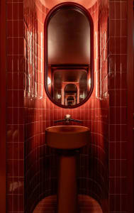 Bathroom with red walls, a metal sink, and two mirrors, creating a warm and inviting atmosphere