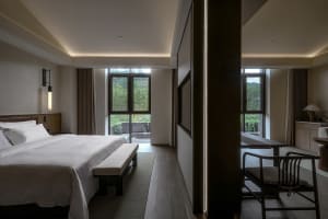 A well-lit bedroom with a large bed on a hardwood floor, two windows, and a warm atmosphere