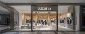 Spacious retail space with a glass door, wood accents, and well-lit atmosphere, featuring mannequins and clothing items