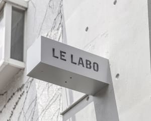 A real photo of a building exterior with white walls, a sign on the side, and natural lighting