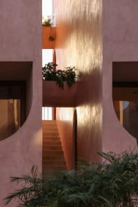 A warm and inviting building with a pink exterior, featuring a staircase leading to a balcony with a plant, and two sets of stairs on either side